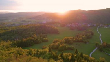 Idyllic kırsal kesim ve sonbahar günbatımı ışınlarında yıkanan köyler. Ağaçlık tepeleri, yeşil otlakları ve sonbahar mevsiminin güzel altın ışığında küçük yerleşim alanları olan resim gibi bir manzara.