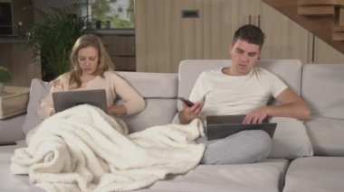 Ev izolasyonu için dizüstü bilgisayar ve akıllı telefon kullanan çift. Karantinadayken iş görüşmeleri yapan evli bir çift ve diğer ofis işleri..