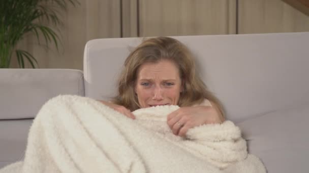 女人在看毛毯覆盖的恐怖片时感到害怕 女士坐在舒适的沙发上看电视 冬夜休闲活动中的女性 — 图库视频影像