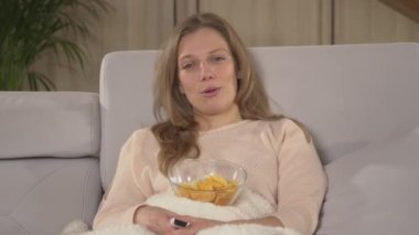 Güzel bir kadın rahat bir kanepede eğleniyor ve romantik komedi izliyor. Battaniyeyle kaplanmış güzel bir bayan film izlerken abur cubur yiyor. Genç bir kadın bir kış akşamında dinleniyor..
