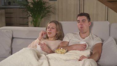 Tatlı bir çift abur cubur yiyor ve komik TV şovu izlerken çay içiyor. Genç çift kanepede oturuyor ve rahat bir sonbahar akşamında evinde film gecesinin tadını çıkarıyor..