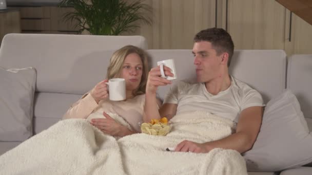 亲密接触 一对年轻夫妇在舒适的沙发上放松一下 看电视 在一个漫长的冬夜 坐在沙发上 铺着毛毯 享受着在家里客厅里放松的电影之夜 — 图库视频影像