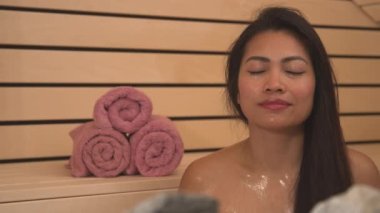 PORTRAIT, Fin saunasında dinlenen güzel genç bayanın vesikalık fotoğrafı. Terli Filipinli kadın sıhhatli sıcak ahşap saunada derin derin nefes alıyor. Genel refah için sağlıklı bir yaşam tarzı