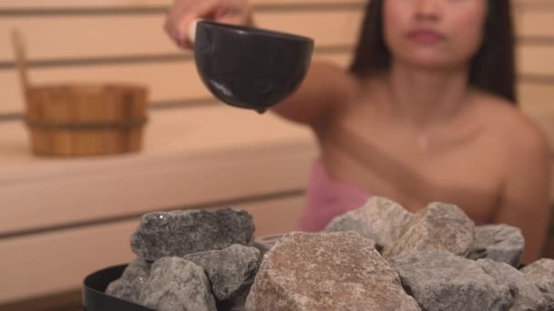 芬兰桑拿浴室的女人们向加热器的石子中倒水 以制造蒸汽 石子作为桑拿蒸汽浴稍慢蒸发的必要设备 美丽的女士用温泉招待自己 — 图库视频影像