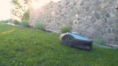 LJUBLJANA, SLOVENIA, HAZİRAN 2022: Yukarı doğru hareket ederken robotik çim biçme makinesi yeşil çimenleri uzaktan buduyor. Bahçe çimlerini biçmek için gelecekten gelen bahçe malzemeleri..