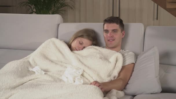 一对年轻夫妇患流感 在病假期间躺在沙发上休息 流鼻涕的男人和睡在他肩膀上的女孩都睡在毯子下 新婚夫妇秋天得了季节性流感 — 图库视频影像