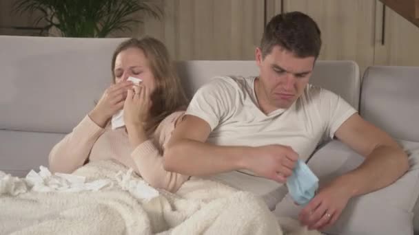年轻女人打喷嚏 然后年轻男人戴上防护面罩 冬季感冒和病毒四处蔓延 已婚夫妇依偎在舒适的沙发上 而女人却感染了季节性的病毒 — 图库视频影像