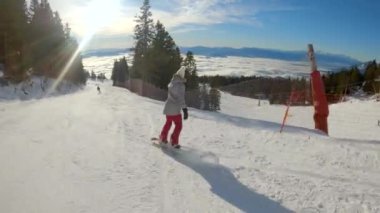 Güneşli bir kış gününde kayakla kayak yapan genç bir kadın. Alp kayak merkezinde kayak ve snowboard yapmak için bir kış masalı. Bayan snowboardcu kış tatilinin tadını çıkarıyor..