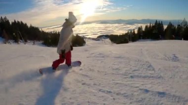 Güneşli bir kış gününde dağ eteklerinde kayak yapan kadın snowboardcu. Kar kayağı ve kayak için mükemmel koşullar. Sisli vadinin üzerindeki muhteşem manzaralı dağlık kayak merkezinde..