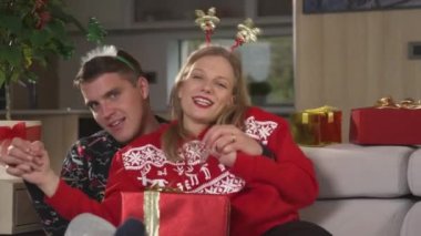 PORTRAIT: Merry couple dancing and singing together while watching Christmas show. Cheerful twosome in Christmas sweaters celebrating holidays and enjoying relaxing festive time on comfortable sofa.