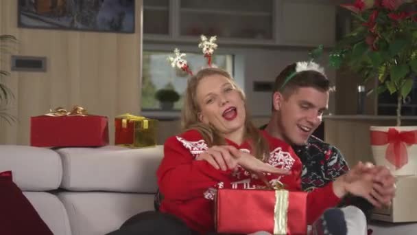 欢乐的男男女女在电视上唱着圣诞歌曲跳舞 身着圣诞毛衣的年轻夫妇在装饰过的客厅里欢度佳节 共度轻松时光 — 图库视频影像