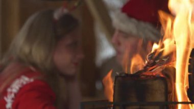 CLOSE UP: Burning flames and cute couple sharing romantic moments on Christmas. View of fireplace and young twosome in love enjoying cosy atmosphere in home living room on festive winter Evening.