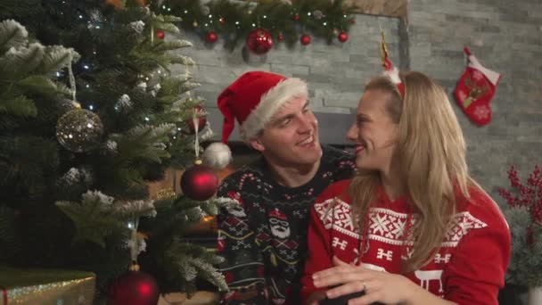 男は贈り物で彼の女性を驚かせたとき かなりのカップルはクリスマスツリーを飾る 若いです男性と女性身に着けていますお祝いの服お祝いクリスマス休暇で美しく装飾された家のリビングルーム — ストック動画