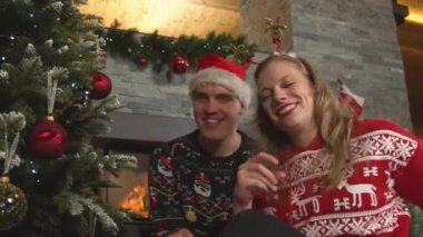 PORTRAIT: Cute cheerful couple dancing and singing together by the Christmas tree. Smiling man and woman in festive dress feeling happy during Christmas celebration and blowing kisses to the camera.