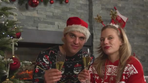 点点滴滴 圣诞前夜 一对欢快的情侣举杯香槟酒祝酒 快乐的男女青年坐在壁炉前的圣诞树旁 一边喝着香槟 一边庆祝 — 图库视频影像