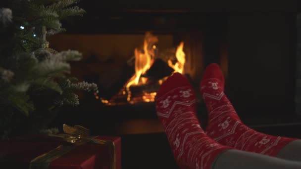 閉じる 女性はクリスマスの靴下に足を揺らし 暖炉で暖まる クリスマスの夜に美しく装飾された自宅のリビングルームの快適さで楽しんでリラックスした女性の人 — ストック動画