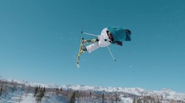 VOGEL, BOHINJ, JULIAN ALPS, SLOVENIA, MARCH 2022: SLOW MOTION: Amazing view of following freestyle skier jumping on big air kicker. Extreme athlete rotating through the air and performing grab trick.