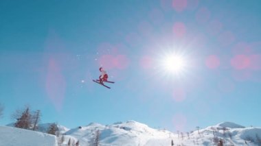 SLOW MOTION: Freestyle skier flying high after jumping big kicker at snow park. Extreme skier double rotating through air and performing grab trick