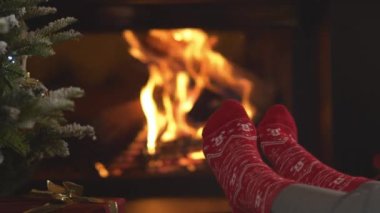 CLOSE UP: Woman's feet in red socks with Christmas pattern by the fireplace. Female person enjoying and resting in relaxing ambiance of her festively decorated home living room on Christmas evening.