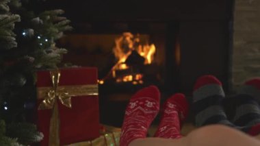 CLOSE UP: Couple wears Christmas socks on their feet and relax by fireplace. Man and woman enjoying and resting in the pleasant ambiance of their warm and festive home living room on Christmas evening