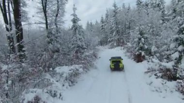 MARCH 2022, LJUBLJANA, SLOVENIA: AERIAL: Amazing performance on Jimny Suzuki 4x4 car driving through snowy forest. Mini 4-wheel drive SUV moving through woodland along snowy winding road on cloudy day