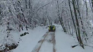 MARCH 2022, LJUBLJANA, SLOVENIA: AERIAL: Beautiful winter drive with Jimny Suzuki 4x4 car through snowy forest. Mini 4-wheel SUV vehicle moving through woodland along snow-covered road on cloudy day.