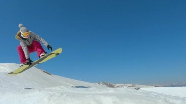 TURRACHER HOHE, ALPS, AUSTRIA, NOVEMBER 2022: SLOW MOTION: Young woman with snowboard jumping kicker at snow park in ski area. Freestyle female snowboarder performing stylish indy grab trick on jump.