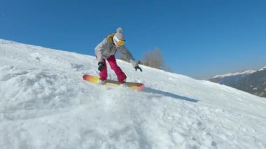 SLOW MOTION: Woman crashes into soft snow while snowboarding on snowy ski slope. Young female snowboarder tries to learn how to turn and ride snowboard at mountain ski resort on a beautiful sunny day.