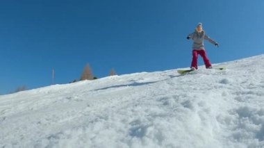 CLOSE UP: Female beginner snowboarder crashes towards camera while snowboarding. Young woman is learning to ride a snowboard and makes a turn when she drops down on snowy slope at mountain ski resort.