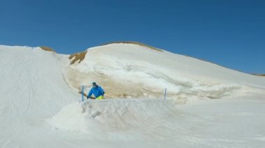 SLOW MOTION: Male snowboarder performs stylish grab trick on jump in snow park. Young man on snowboard doing melon grab while jumping on big kicker at freestyle park at snowy mountain ski resort.
