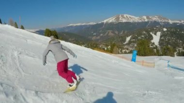 Girl snowboarder falls back on snow while learning to snowboard on ski slope. Young woman landing in snow after losing balance while snowboarding down the piste at snow-covered mountain ski resort.