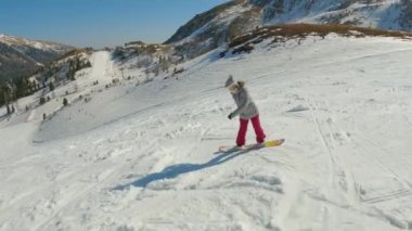 Woman taking her first beginner turns on a snowboard when she crashes on snow. Young lady landing in snow after losing balance while snowboarding down the slope at snow-covered mountain ski resort.