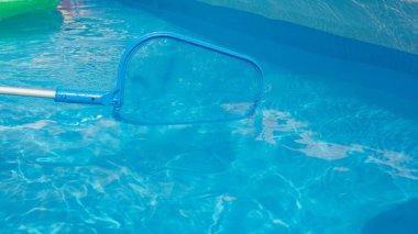 CLOSE UP: Unrecognizable pool cleaner uses a leaf net during seasonal maintenance works. Plastic pool skimmer cleans up tiny leaves from the glassy pool water. Person cleaning pool in the backyard