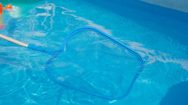 CLOSE UP: Unrecognizable person is cleaning pool in the backyard. Pool cleaner uses a leaf net during seasonal maintenance works. Plastic pool skimmer cleans up tiny leaves from the glassy water.