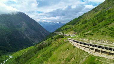 Parlak yeşil İsviçre Alplerinde kapalı bir dağ geçidi boyunca uçan AERIAL. Simplon Geçidi 'nin İsviçre' nin pitoresk dağlarındaki sinematik insansız hava aracı bakış açısı. Dağ boyunca manzaralı rota