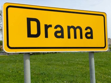CLOSE UP: Funny shot of a signpost showing traffic they are arriving into Drama village. A yellow traffic sign indicates you are entering the amusingly named town of Drama in Slovenian countryside.