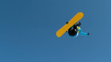 BOTTOM UP: Athletic male tourist snowboarding in the gorgeous Japanese mountains jumps into the air and performs a spinning grab trick. Spectacular shot of a young male snowboarder catching big air.