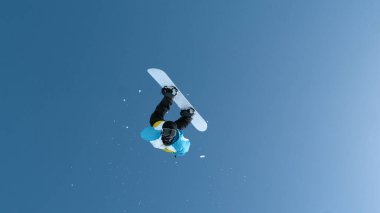 Fearless young male snowboarder does a breathtaking backflip after jumping off a massive kicker. Man snowboarding in the Chinese mountains performs a spectacular flip while riding in a snowboard park.