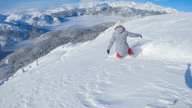 Woman on active vacation in the Slovenian mountains snowboards in the backcountry. Extreme female snowboarder shreds fresh powder snow while riding off-piste in the sunny Julian Alps.