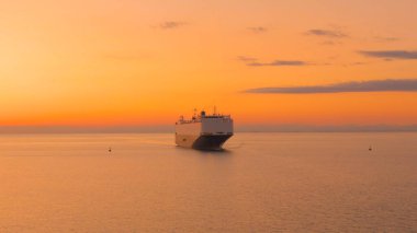 Büyük kargo gemisi sonsuz sakin okyanusu aşarak güneşli bir akşamda büyük bir uluslararası limana doğru yelken açıyor. Büyük bir yük gemisi, altın gün batımında ağır kargo taşıyor..