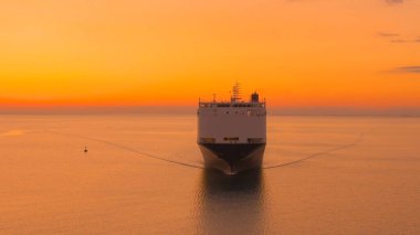 AERIAL: Golden summer evening sky spans above a freight ship transporting goods across the tranquil ocean. Scenic drone point of view of a massive cargo carrier sailing across the sea at sunset.