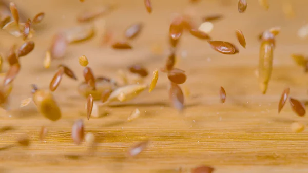 Macro Dof 空のキッチンカウンター越しに跳ねる小さなシリアル種の高詳細ビュー 乾燥小麦 光沢のある茶色の亜麻の種の混合物は 木製のダイニングテーブルに散在します — ストック写真