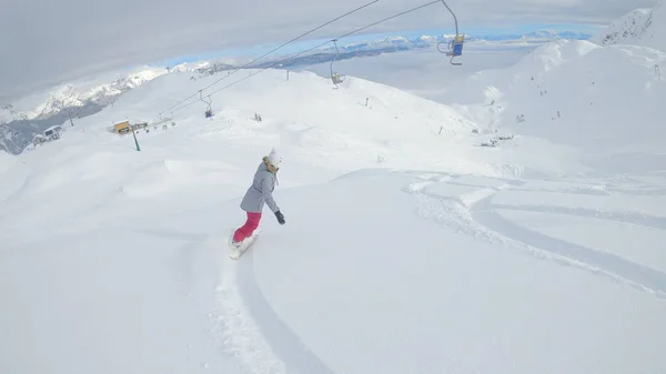Unrecognizable female snowboarder rides off piste on a perfect winter day in the picturesque Julian Alps. Woman on active winter vacation snowboards cross country and shreds freshly fallen powder snow