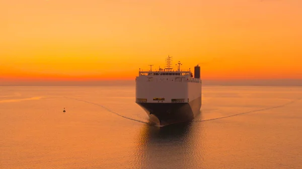 航空宇宙 日没時に商品を輸送する貨物船の壮大なドローンショット 大型貨物船が豪華な黄金の夕日で重い貨物を輸送しています 産業用船舶の近くを飛ぶ — ストック写真