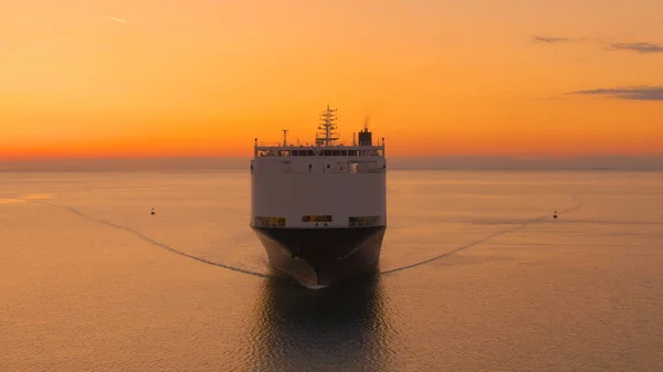 大きな貨物船は絵のように燃えるオレンジ色の日の出で穏やかな海を航海しています 晴れた夏の夜に商品を輸送する国際貨物船の前を飛ぶ — ストック写真