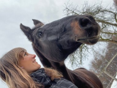 SELFIE: Young Caucasian woman lovingly looks at her beautiful dark brown horse after a long ride in the wintry countryside. Beautiful selfie shot of a female rider bonding with her majestic stallion.