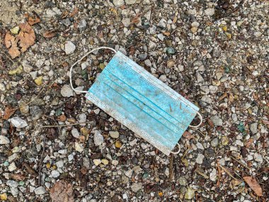 CLOSE UP: Covid-19 pandemic is polluting the environment with protective masks. Dirty disposable surgical facemask lies on the wet gravel ground. Facemask is left on the ground during autumn lockdown.