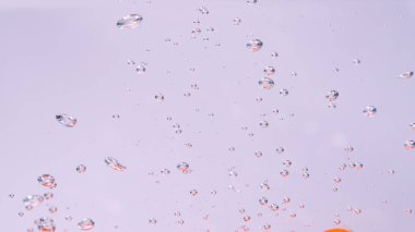 CLOSE UP, UNDERWATER, DOF: Tiny air bubbles rise up as a ripe red cherry tomato is dropped into the refreshingly cold tap water. Bubbles of air float up to the surface of the crystal clear water.