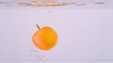 CLOSE UP, UNDERWATER: Fragrant red and yellow apple falls into the crystal clear fresh water. Cinematic shot of a small homegrown apple falling and splashing into the refreshingly cold fresh water.