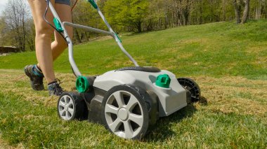 CLOSE UP: Female gardener using lawn aerator to grow healthier and thicker lawn. Spring backyard garden work for lawn growth enhancement. Practical gardening machinery for efficiency at landscaping.